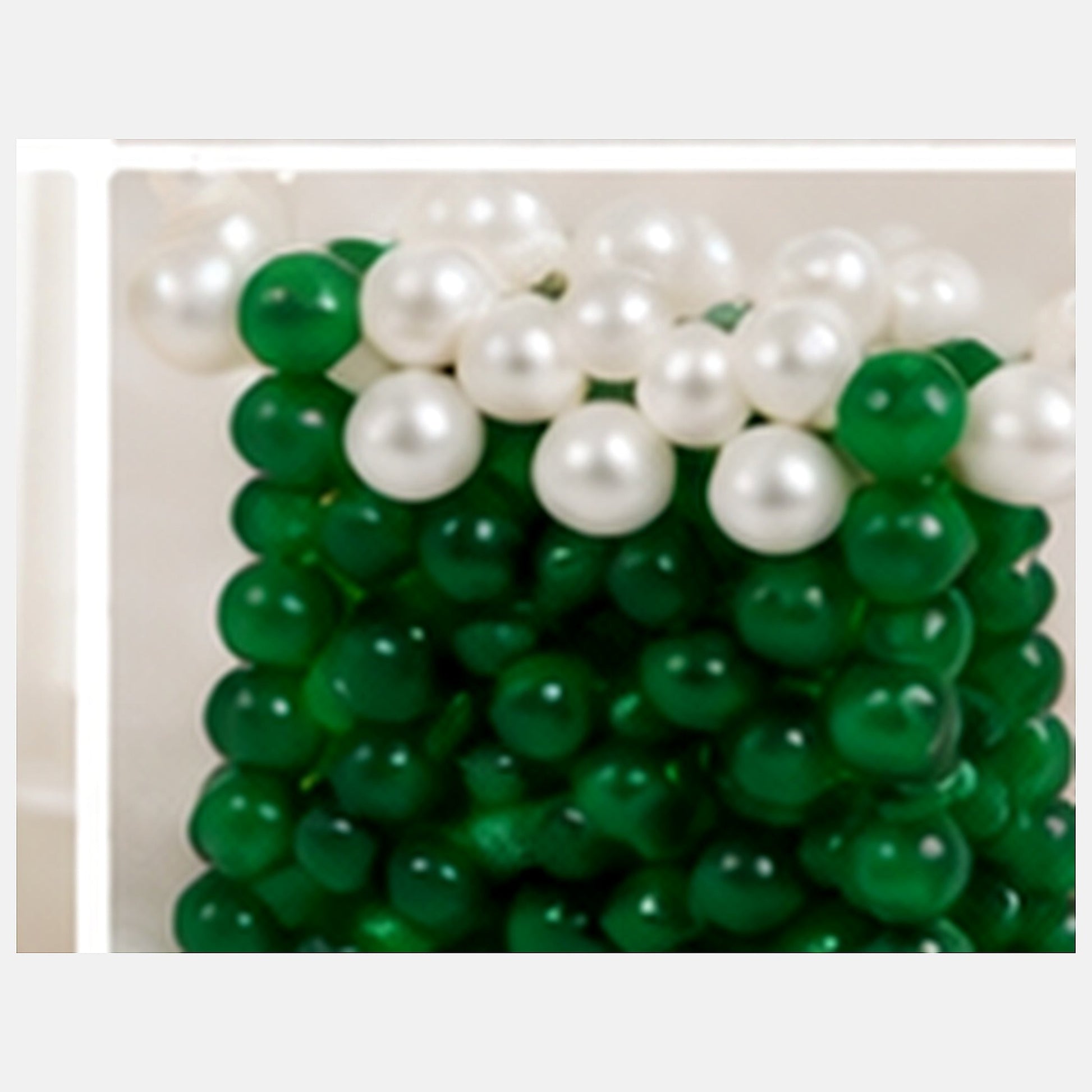 Macro close-up of glossy green beads, white pearl-look beads and woven construction on the mini purse